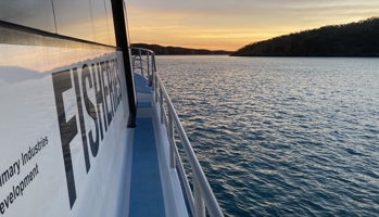 View from boat side rail with scenic view of water and land in the background with orange sunset