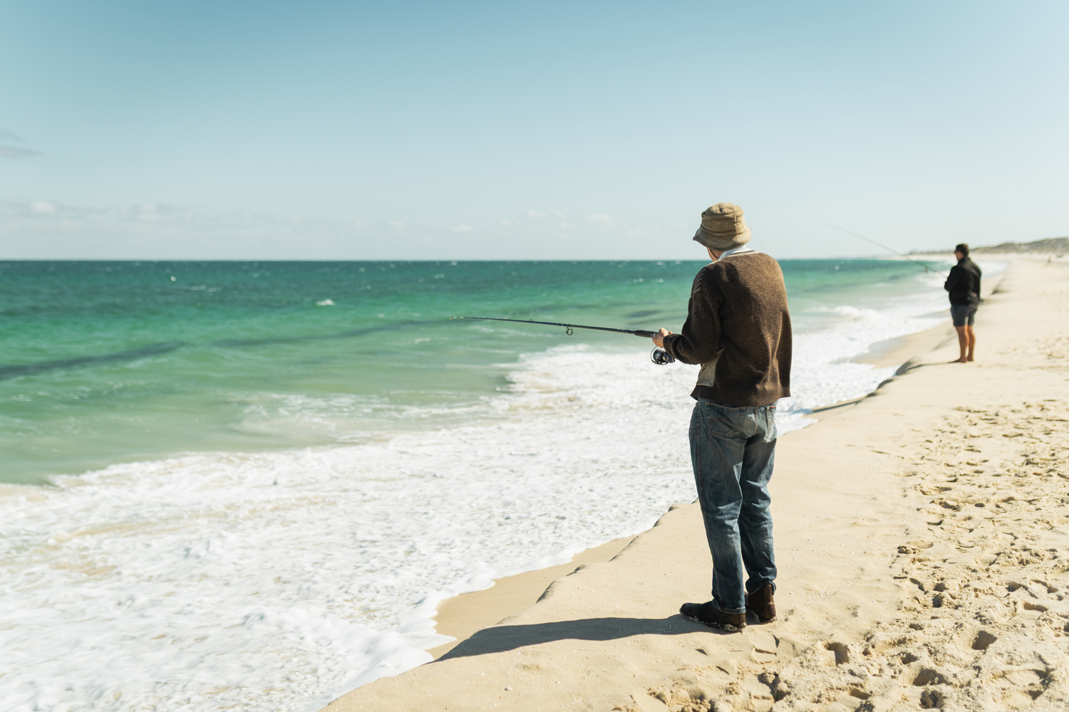 Man standing on beach holding a fishing rod.